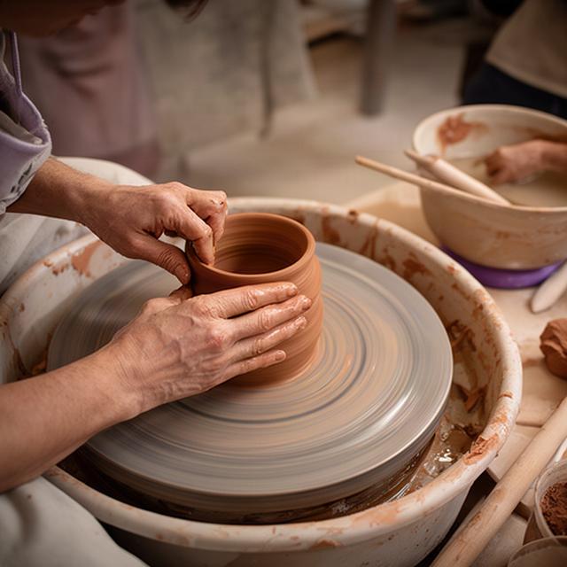 Mani che modellano un vaso sul tornio in ceramica durante una lezione