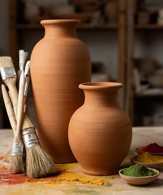 Due vasi artigianali color terracotta accanto a pennelli e pigmenti