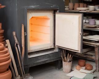 Forno ceramico aperto nell'atelier con piastrelle e strumenti accanto